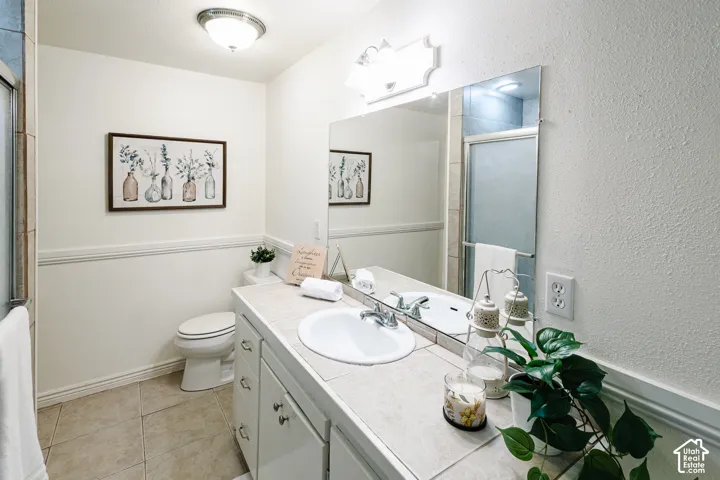 Bathroom featuring a vanity with a tile countertop, integrated basin, large wall-mounted mirror, and tile flooring