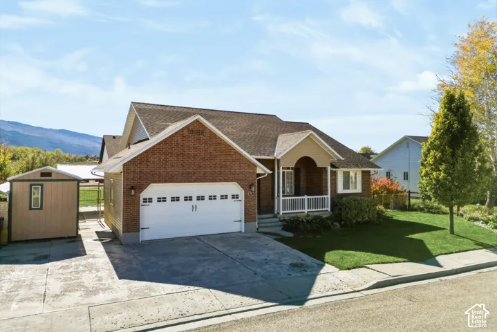 Brick and siding exterior featuring an attached two-car garage, covered front porch with white railing, and an exterior storage shed