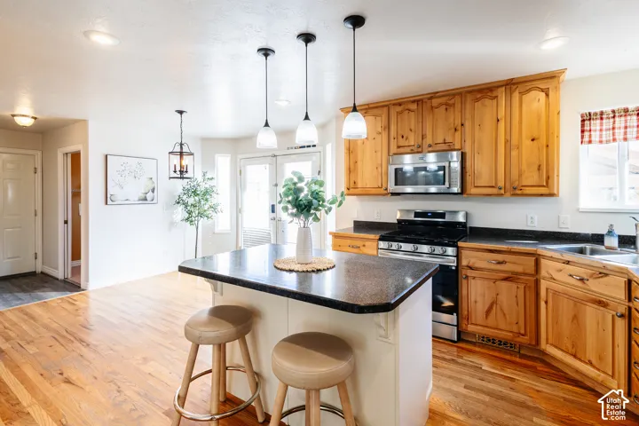 Kitchen featuring natural finish cabinetry, a center island with countertop seating, dark solid-surface countertops, stainless steel appliances, and wood-finish flooring