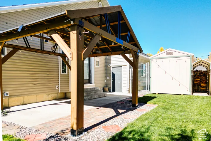 Backyard featuring a wood-frame pavilion with a metal roof, concrete patio, paver accents, and a detached storage shed