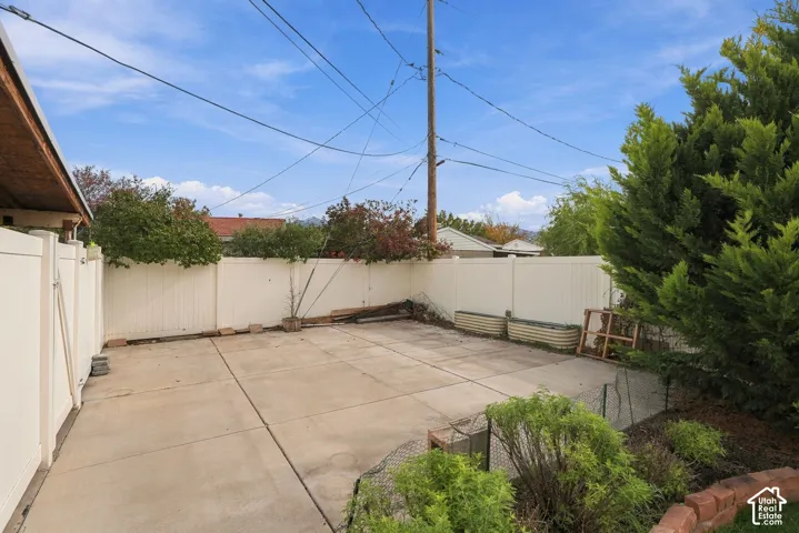 Concrete patio enclosed by a white vinyl privacy fence, featuring raised garden beds and mature landscaping