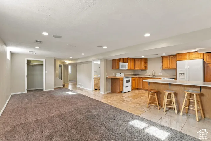 Open-concept interior featuring wall-to-wall carpeting, stone-finish tile flooring, wood cabinetry, a breakfast bar, and recessed lighting