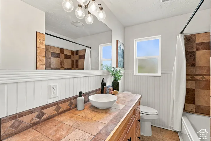 Bathroom vanity featuring a vessel sink, tile countertop, beadboard wainscoting, and large-format tile shower surround