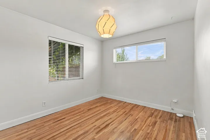 Room featuring wood-finish flooring, dual windows with horizontal blinds, and a geometric pendant light fixture