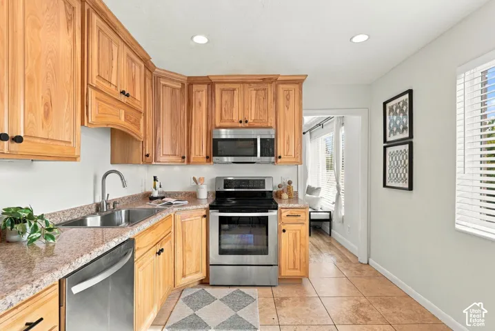 Kitchen featuring natural wood cabinetry, stainless steel appliances, speckled stone-surface countertops, recessed lighting, and tile flooring
