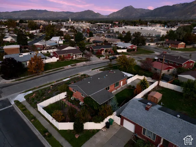 Aerial perspective of a brick residence featuring a fenced backyard, mature landscaping, and mountain backdrop