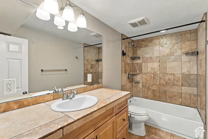 Bathroom vanity with natural stone countertop, undermount sink, multi-light fixture, and tile shower surround