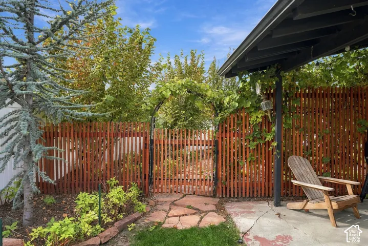 Covered patio featuring a concrete slab and overhead beam support, flagstone walkway, decorative wood picket fencing, and metal garden arbor