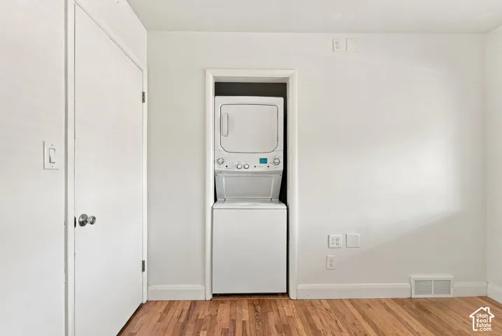 Laundry space featuring a stacked washer and dryer unit, wood-finish flooring, and a solid-core interior door