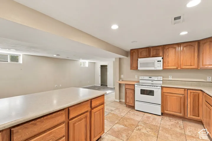 Kitchen featuring natural wood cabinetry, a central island with a solid surface countertop, tile flooring, and integrated white appliances