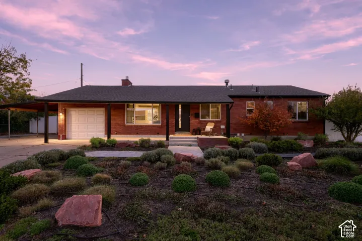 Single-story brick exterior featuring a covered carport, multi-pane windows, a concrete walkway, and landscaped grounds with decorative stone accents