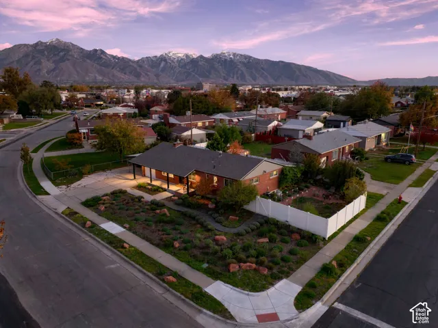 Single-level brick residence featuring a covered front porch, a corner lot location, a white vinyl privacy fence, and a mountain backdrop