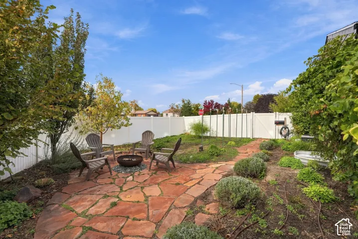 Private backyard featuring a flagstone patio, white vinyl privacy fencing, mature trees, and established garden beds