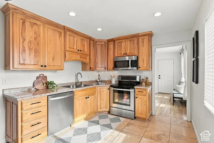 Kitchen featuring natural finish wood cabinetry, stone-texture countertops, stainless steel appliances, and tile flooring