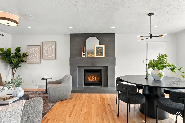 Floor-to-ceiling fireplace featuring a dark stone facade and integrated hearth, complemented by wood-finish flooring, recessed lighting, and a modern multi-arm chandelier