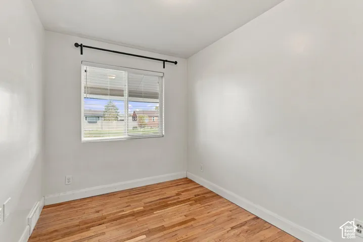 Interior space featuring wood-finish flooring, white walls, and a single-pane window with installed horizontal blinds and a black curtain rod