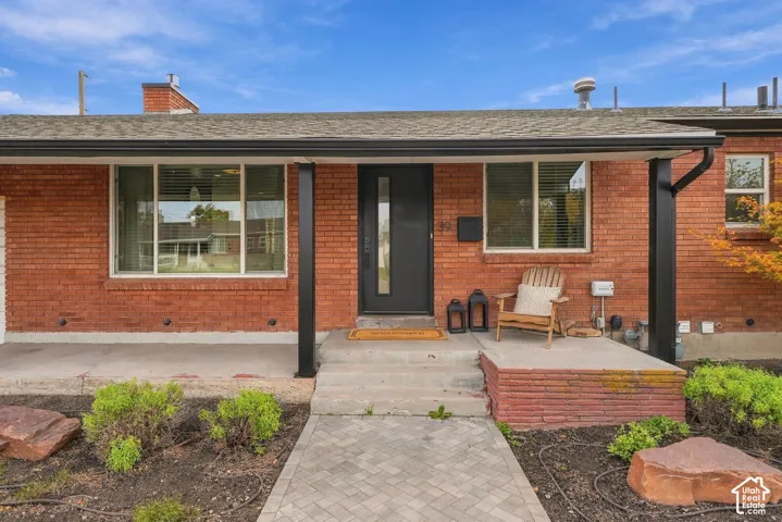 Red brick exterior featuring a covered front porch, concrete steps, a modern front door with vertical glass inlay, and an interlocking paver walkway