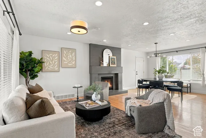 Open-concept interior featuring light wood-finish flooring, a floor-to-ceiling fireplace with a textured grey facade, recessed lighting, and a modern tiered drum pendant light fixture