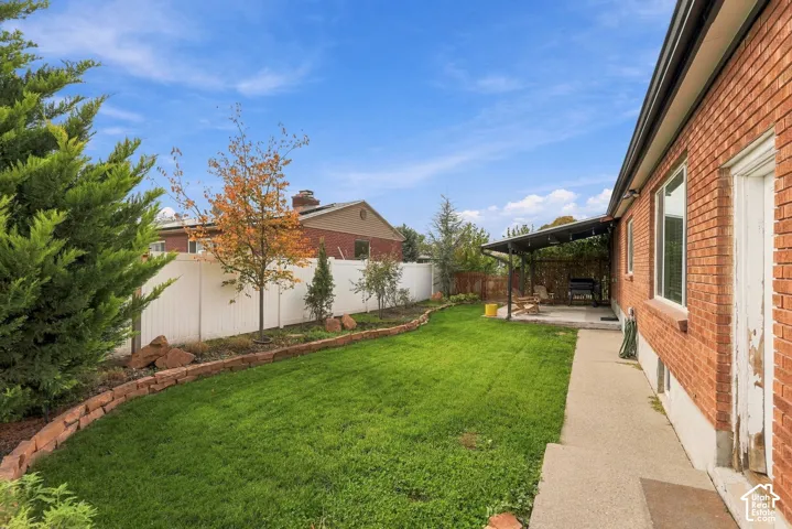 Brick exterior with a covered concrete patio, landscaped garden beds, stone edging, and a perimeter privacy fence