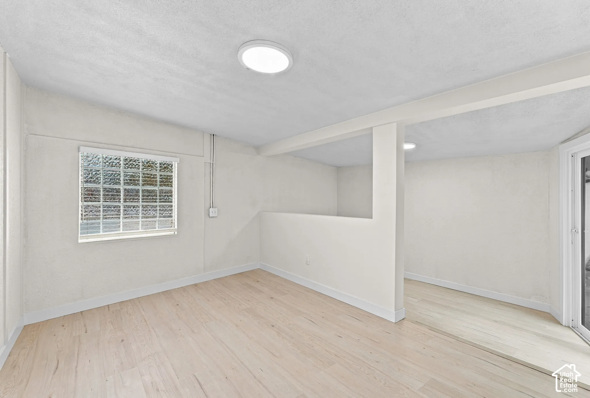 Interior space featuring light-toned wood-finish flooring, glass block window, neutral textured wall finishes, and recessed ceiling lighting