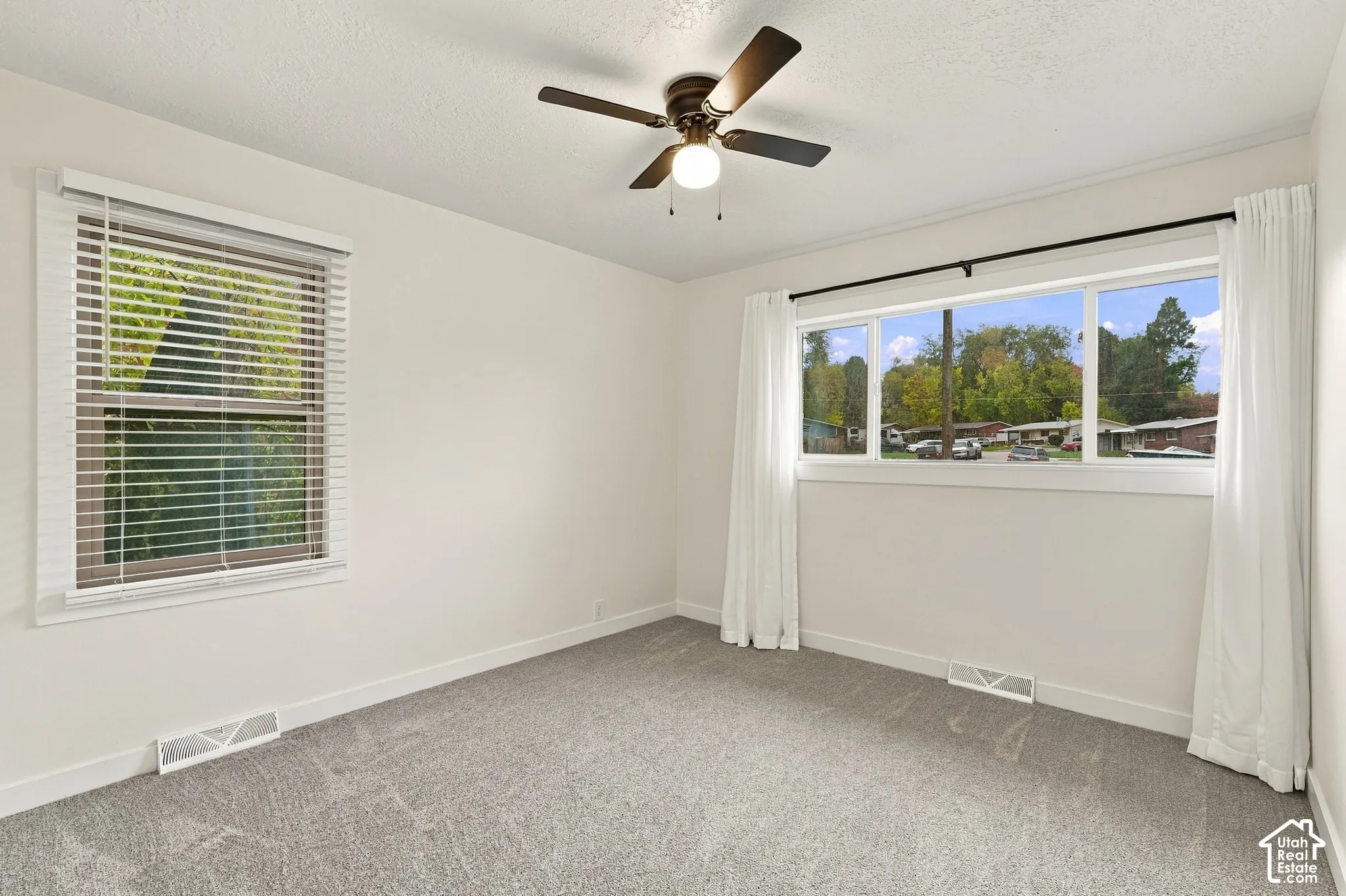 Neutral-toned wall-to-wall carpeting, dual-pane windows with horizontal blinds, and a central ceiling fan with integrated lighting