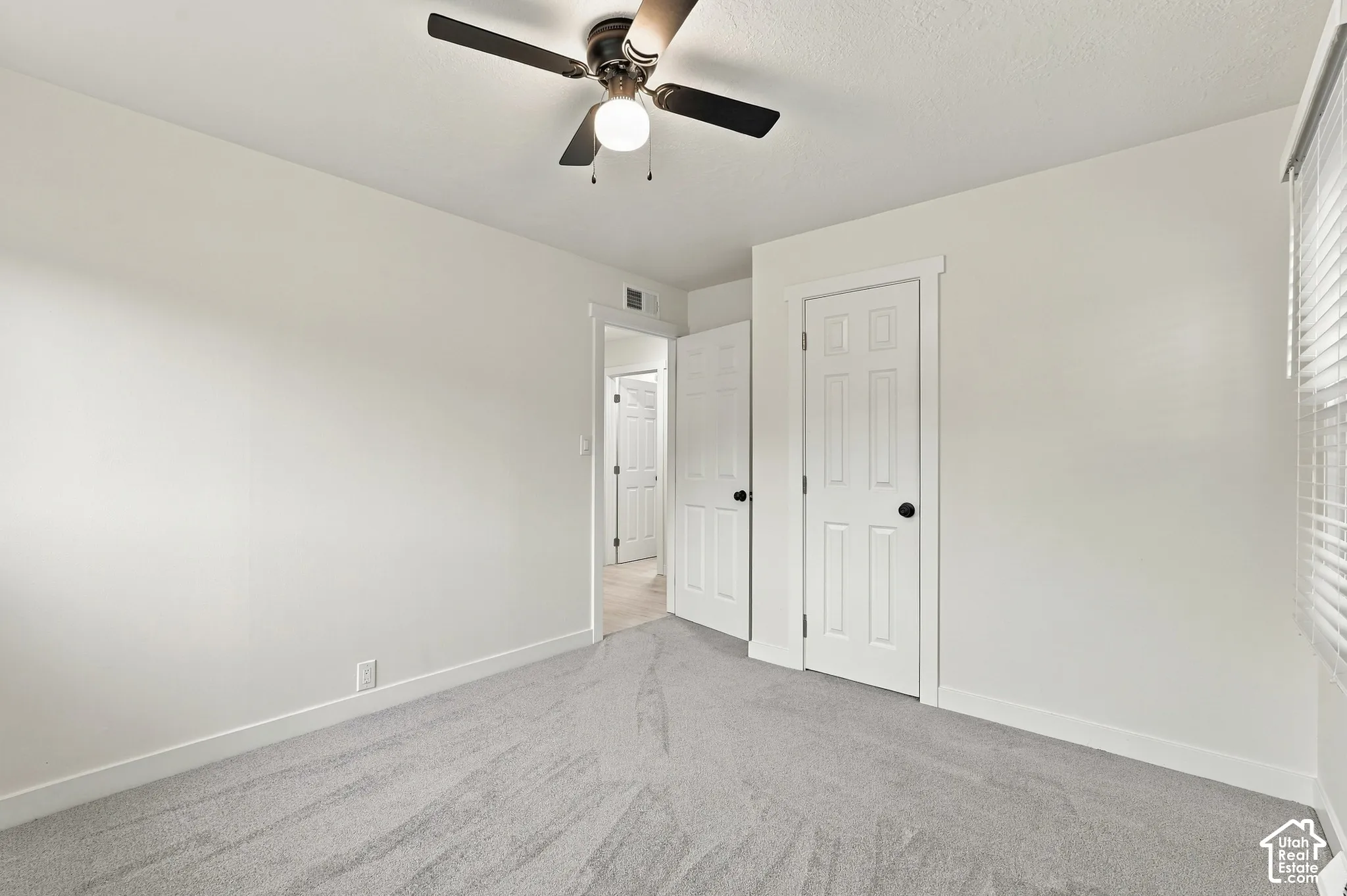 Neutral-toned carpeting, ceiling-mounted light fixture with a fan, and six-panel doors