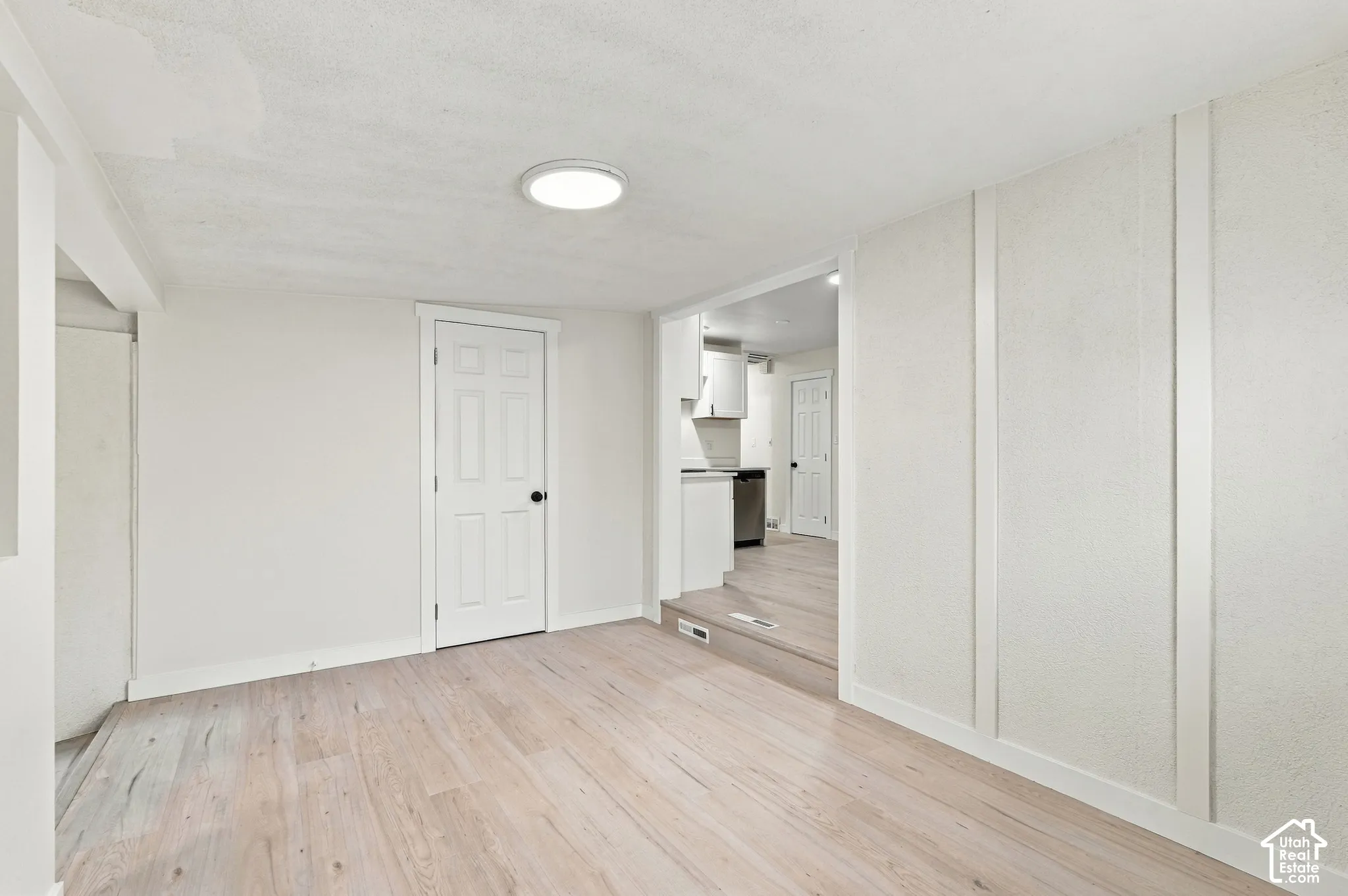 Light-toned wood-finish flooring, vertical wall molding, recessed ceiling lighting, and a solid-core interior door