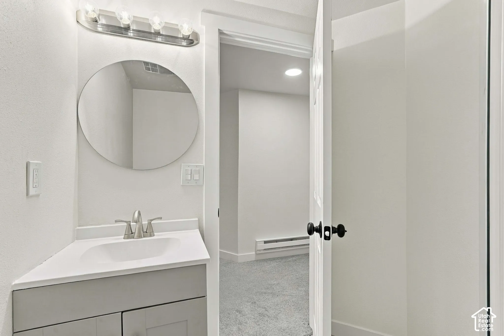 Bathroom featuring a vanity with a white countertop and integrated sink, a circular mirror, and a multi-bulb light fixture
