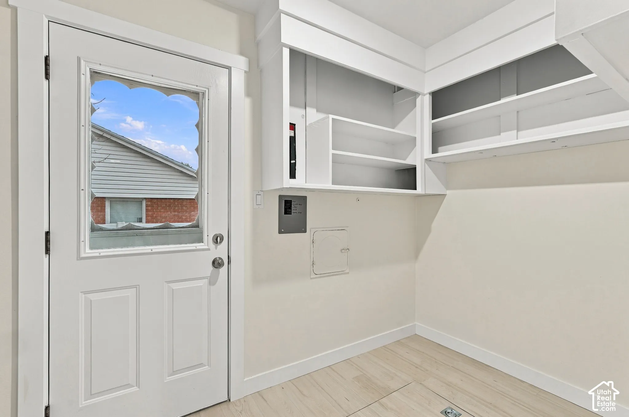 White painted exterior-style door with scalloped glass insert, custom built-in white cabinetry with open shelving, and wood-finish flooring