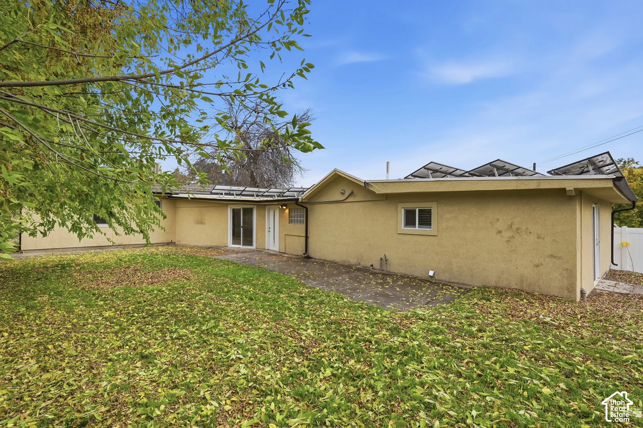Rear exterior featuring stucco siding, rooftop solar panels, a concrete patio, and a sliding glass door