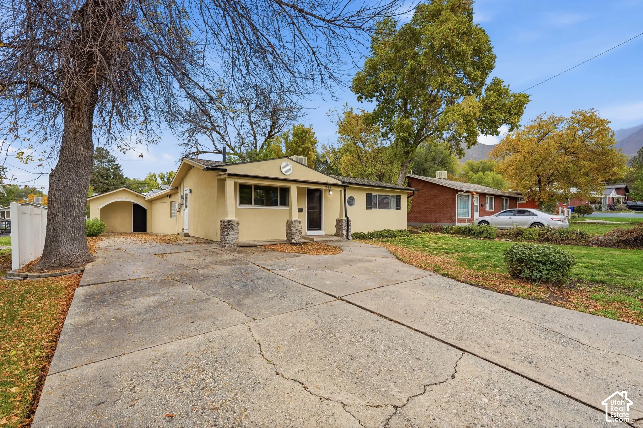 Single-story stucco exterior featuring stone masonry porch columns, a concrete driveway, and an attached carport
