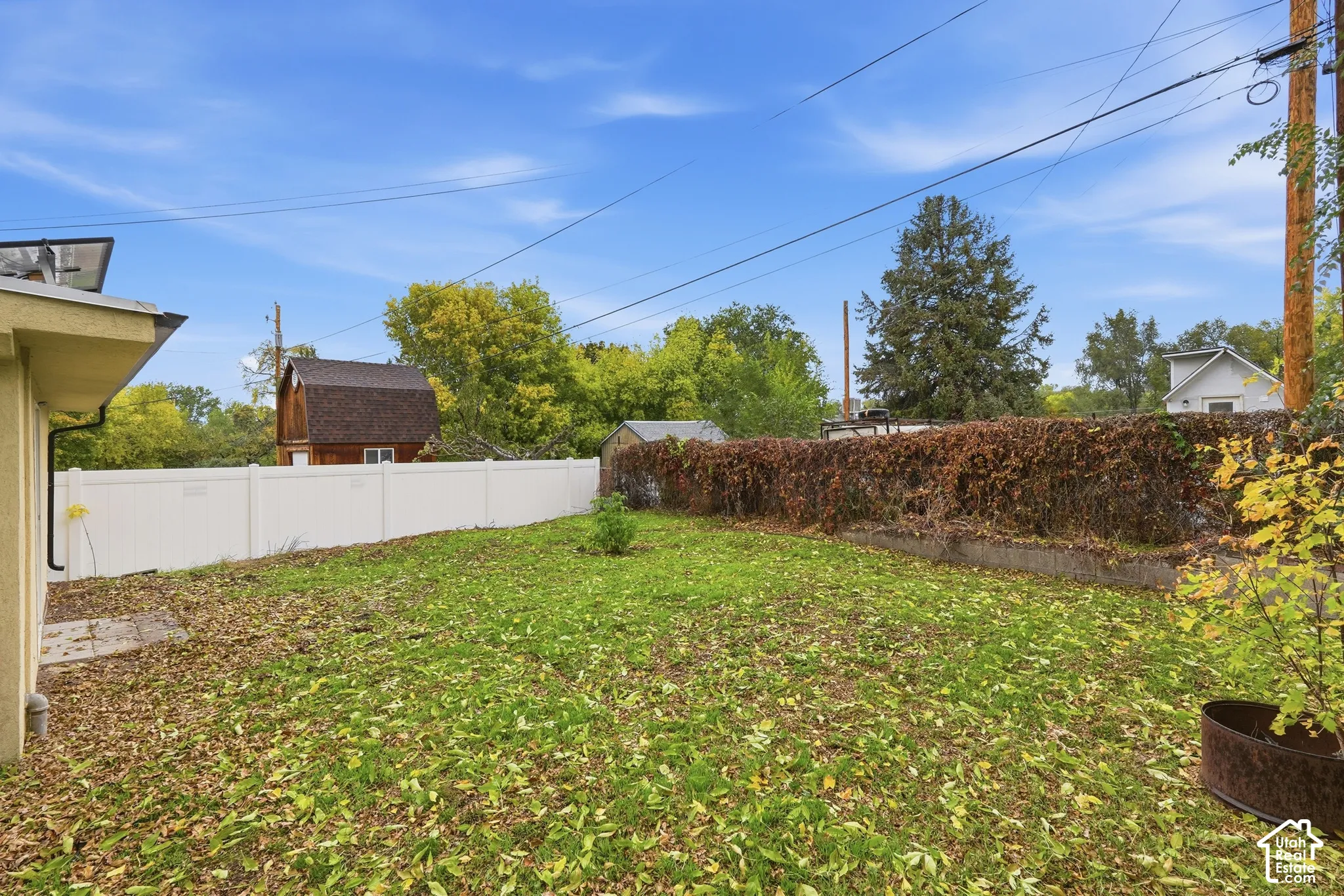 Backyard featuring a white vinyl privacy fence, raised stone wall planter, and mature trees