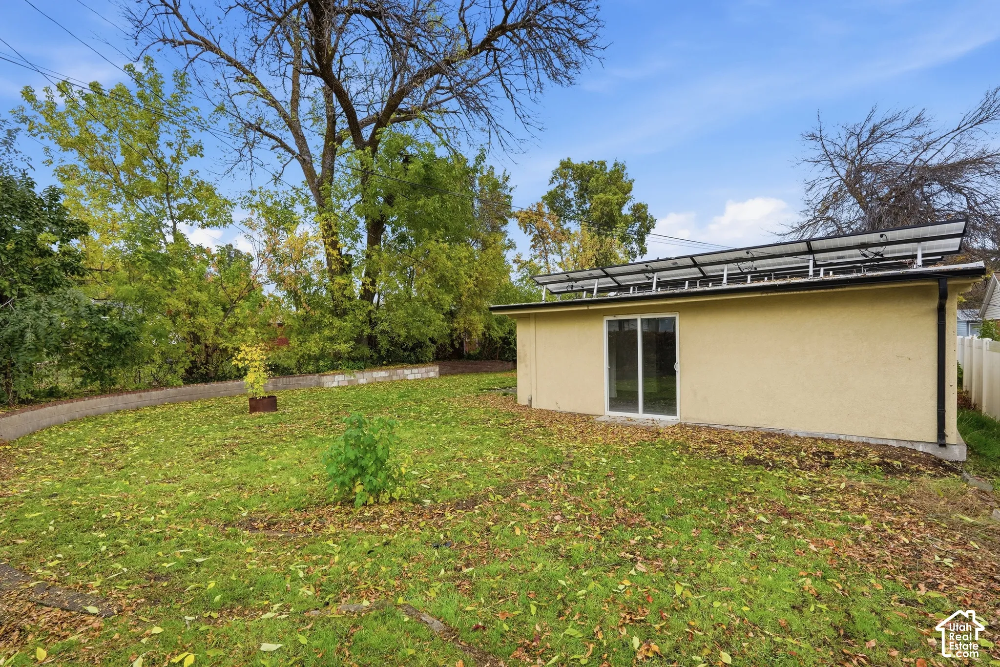 Rear exterior featuring stucco siding, rooftop solar panels, sliding glass door, and a grass-covered lot with mature trees