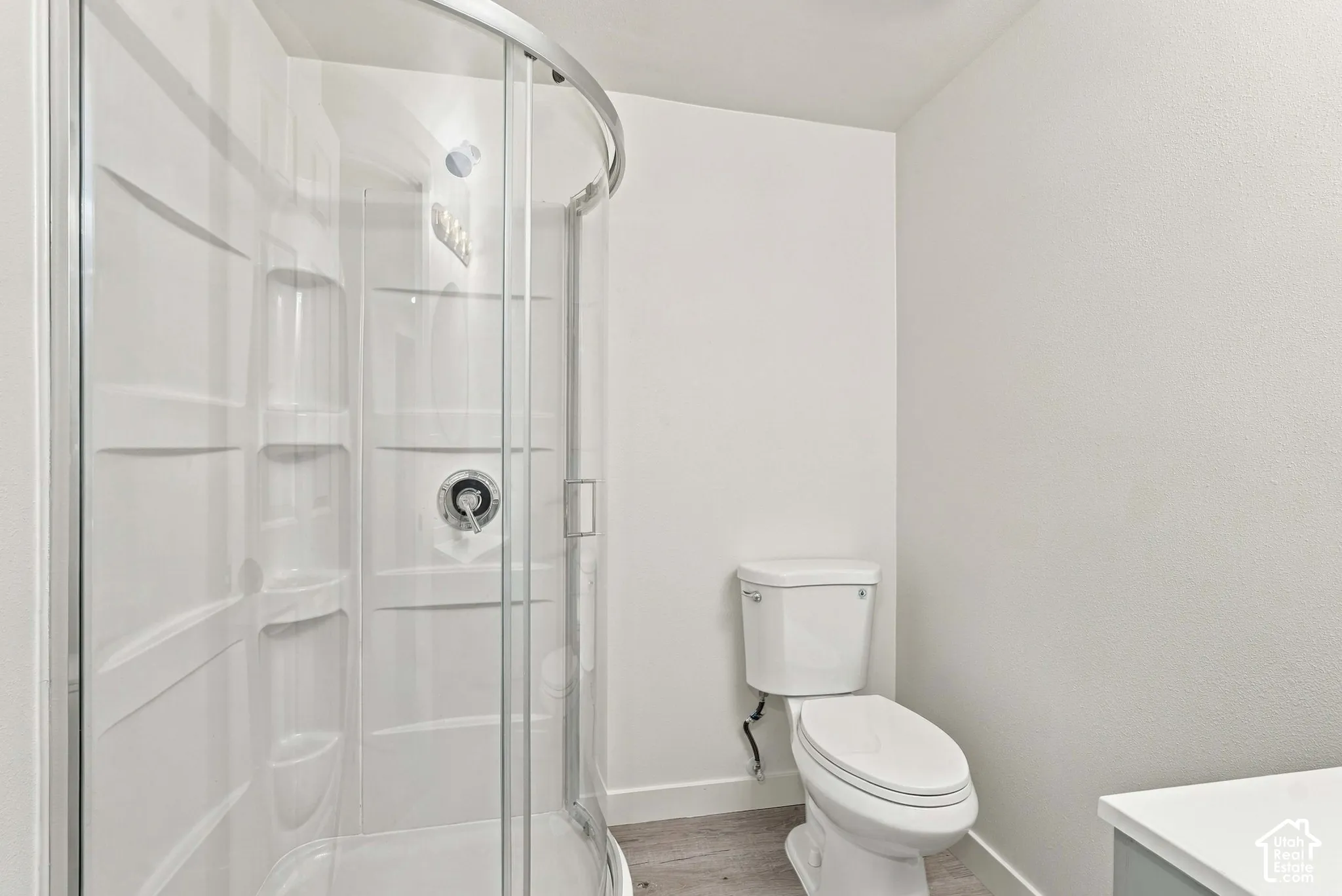 Curved glass-enclosed shower stall with integrated shelving, chrome-finish shower hardware, and dual-flush toilet