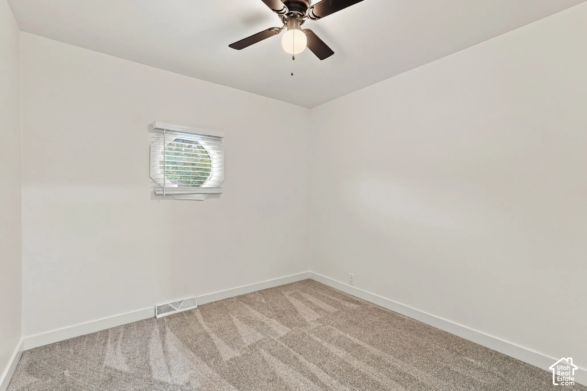 Interior space featuring neutral-toned carpeting, a circular window with fitted blinds, and a multi-blade ceiling fan with integrated lighting