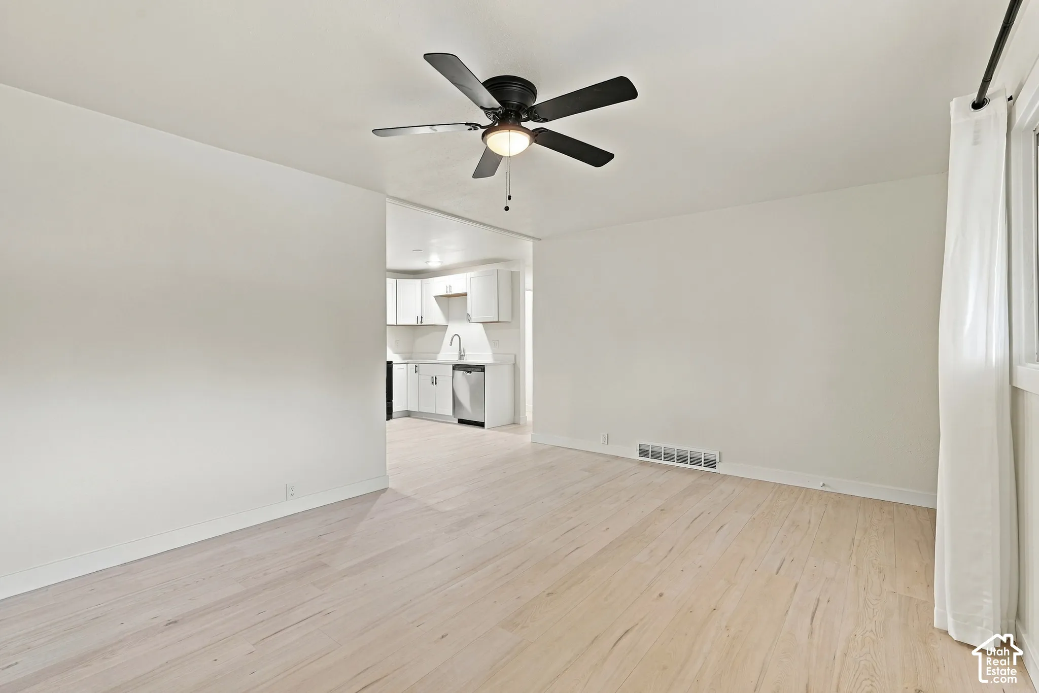 Light-toned wood-finish flooring, matte black ceiling fan with integrated lighting, and white shaker-style cabinetry
