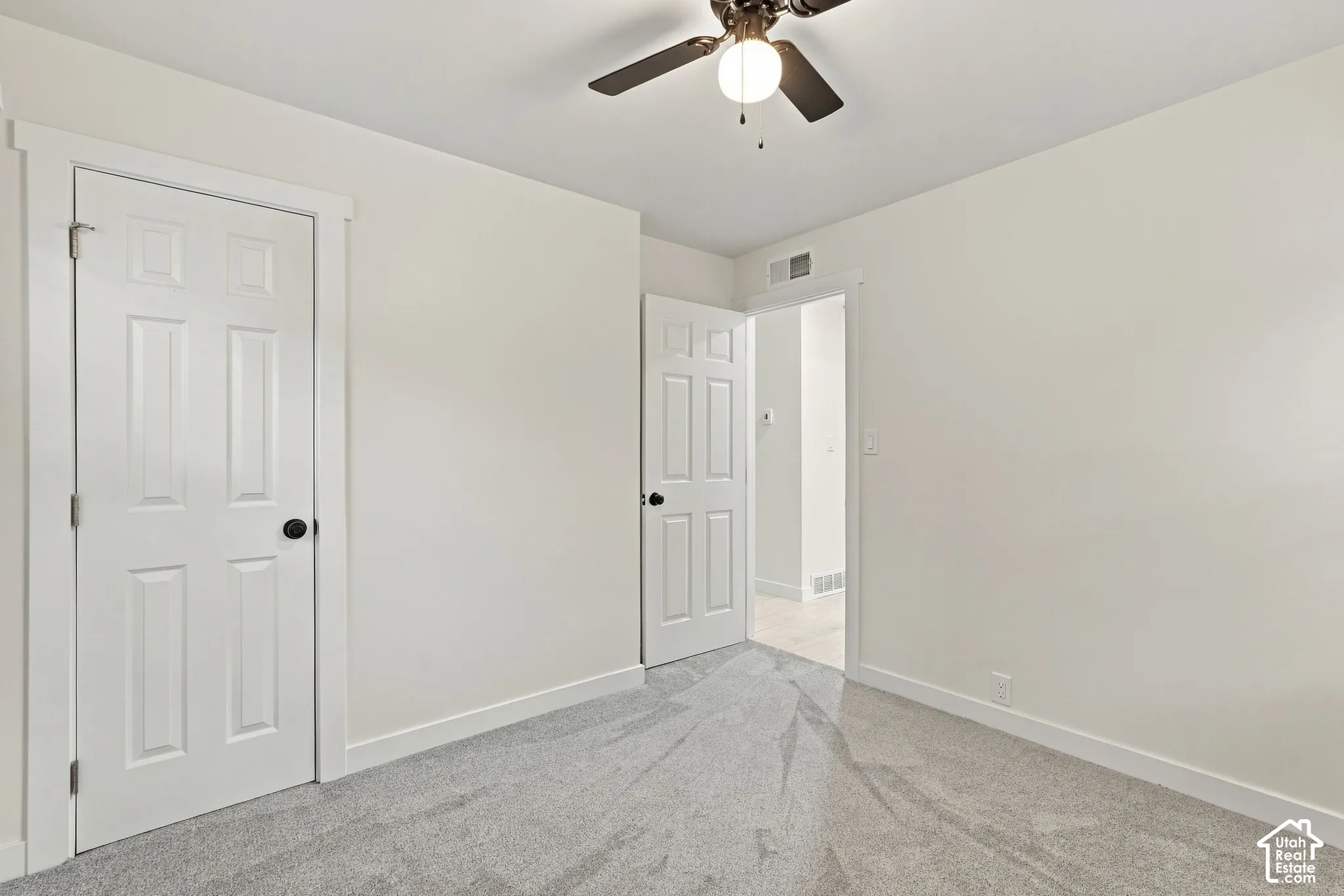 Interior room featuring wall-to-wall carpeting, two six-panel interior doors, and a ceiling-mounted light fixture with a fan