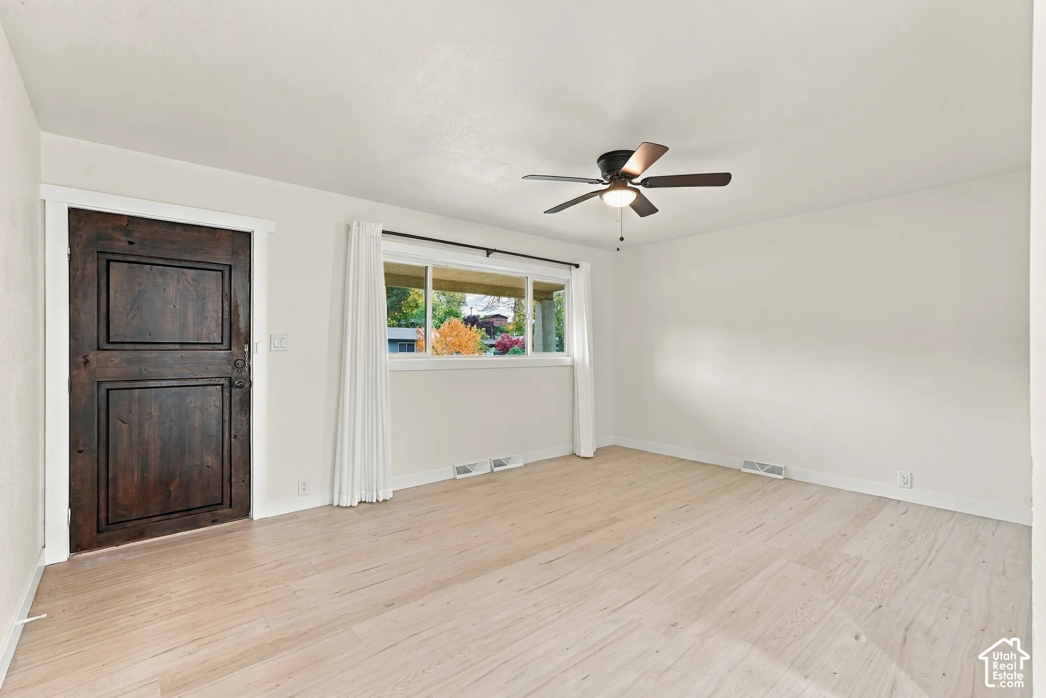 Interior space featuring light-toned wood-finish flooring, a dark-stained paneled door, and a ceiling fan with integrated lighting