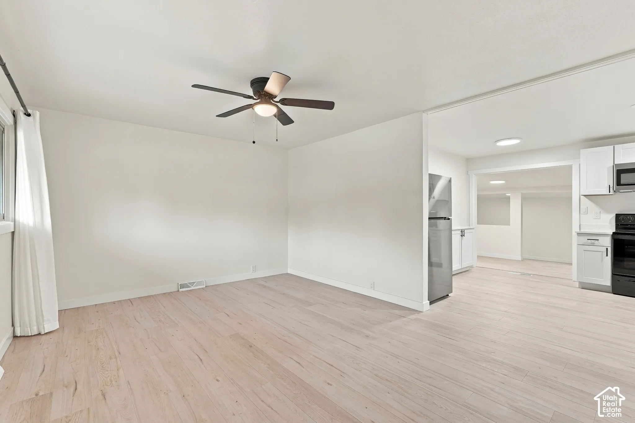 Light-toned wood-finish flooring, ceiling fan with integrated lighting, white shaker-style cabinetry, and stainless steel kitchen appliances