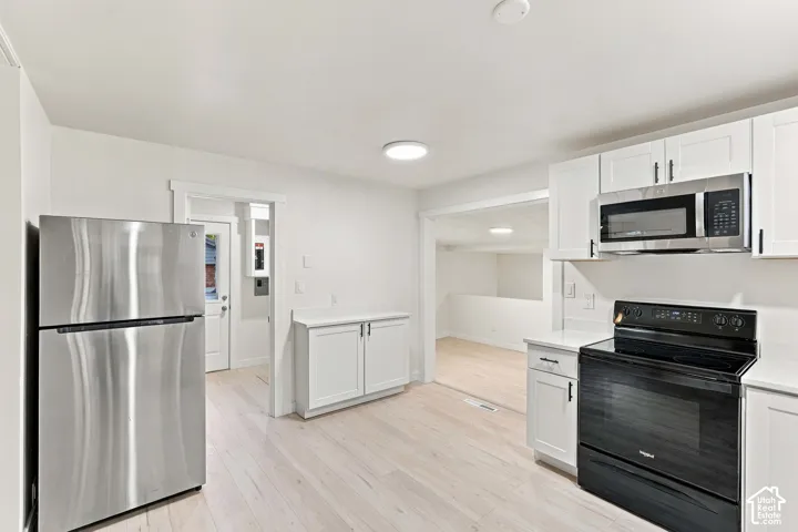 Kitchen featuring white Shaker-style cabinetry, light-toned wood-finish flooring, stainless steel refrigerator, black electric range, and over-the-range microwave