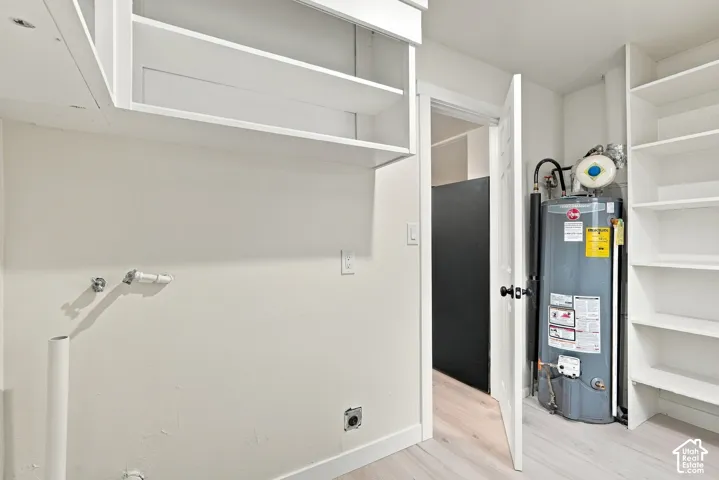 Dedicated utility area featuring white built-in shelving, overhead cabinetry, and a water heater