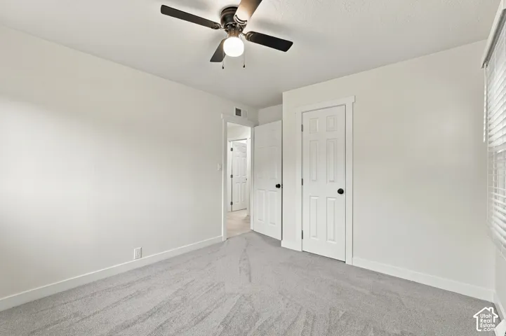 Neutral-toned carpeting, ceiling-mounted light fixture with a fan, and six-panel doors