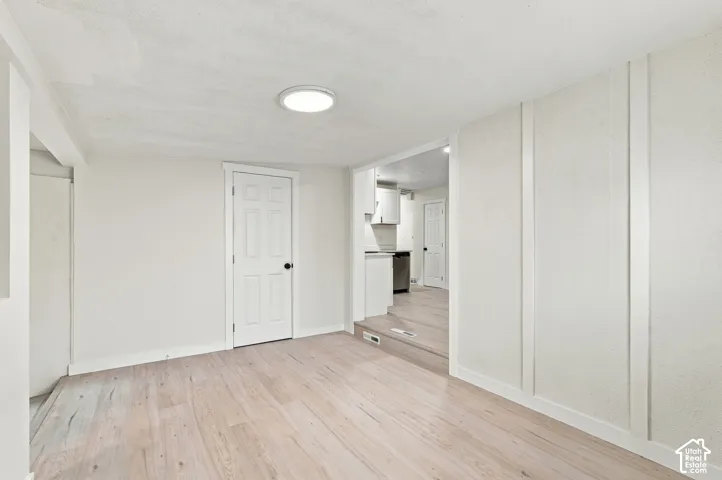 Light-toned wood-finish flooring, vertical wall molding, recessed ceiling lighting, and a solid-core interior door