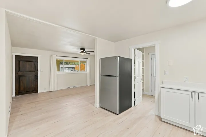 Light-toned wood-finish flooring, white cabinetry with stone-surface countertops, stainless steel refrigerator, and dark wood paneled entry door