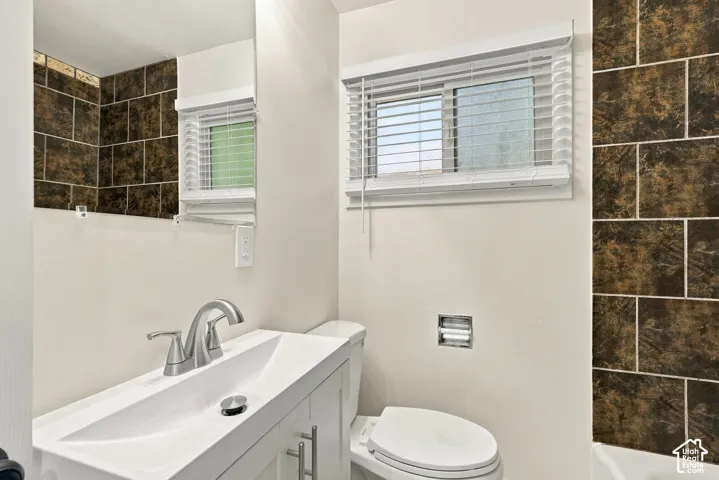 White vanity featuring a rectangular integrated sink with a brushed-nickel faucet, complemented by dark-toned decorative wall tile and a recessed chrome toilet paper holder