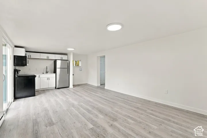 Kitchenette featuring white cabinetry, stainless steel refrigerator, black range, and wood-finish flooring with sliding glass door access