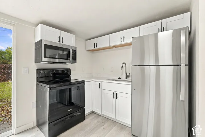 Kitchen featuring white shaker-style cabinetry, stainless steel appliances, a pull-down kitchen faucet, and wood-finish flooring