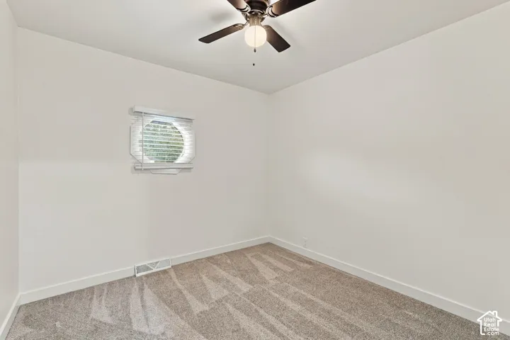 Interior space featuring neutral-toned carpeting, a circular window with fitted blinds, and a multi-blade ceiling fan with integrated lighting