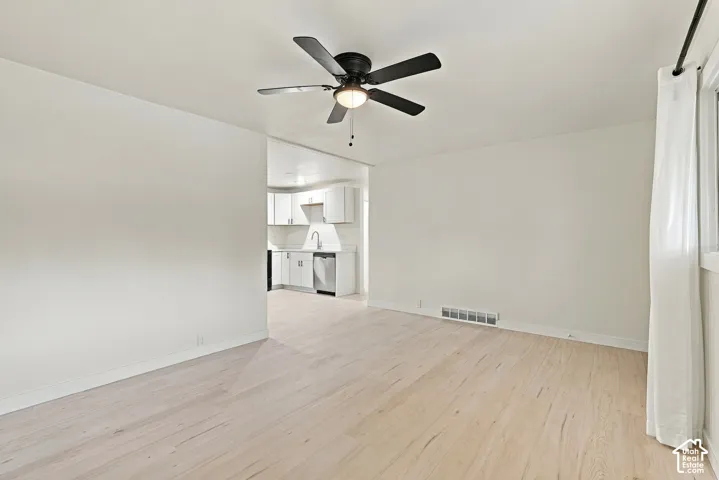 Light-toned wood-finish flooring, matte black ceiling fan with integrated lighting, and white shaker-style cabinetry