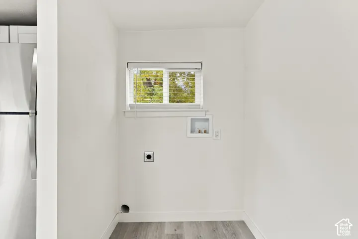 Utility area featuring wood-finish flooring, a single window with horizontal blinds, dedicated water hookups, and a wall-mounted drainage outlet